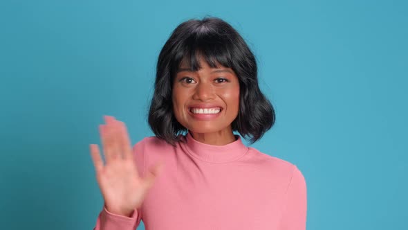 Friendly Woman Says Hello and Waves Hand To Welcome Friends Smiles Broadly