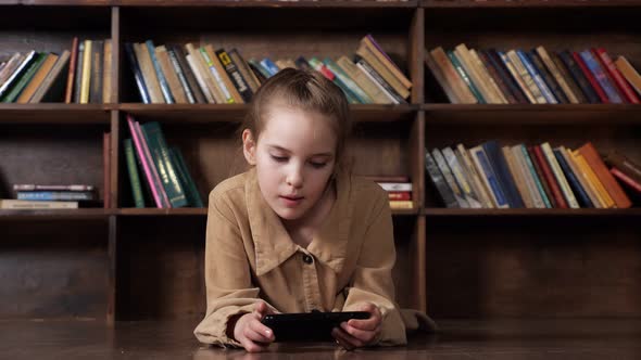 Interested Schoolgirl Plays Online Game on Black Smartphone