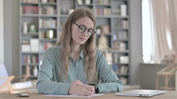Serious Woman Writing On Paper While Sitting in Office
