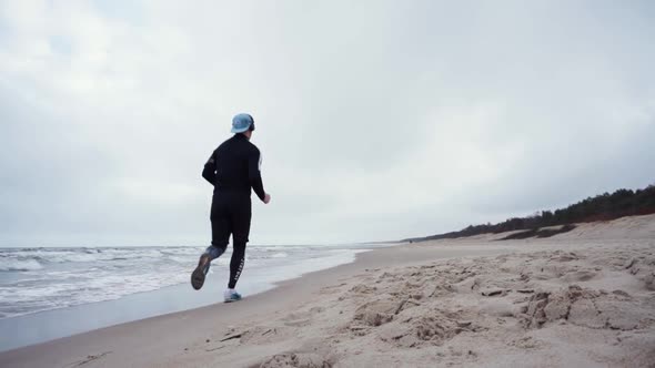 runner with black sportswear is running in the beach away from camera.