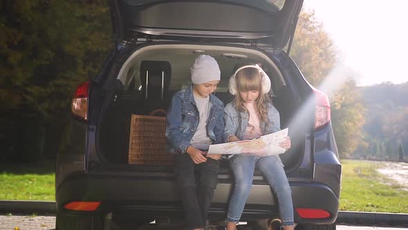 Lovely Teen Children Sitting in the Trunk and Looking at Roadmap Before their Family Car Trip