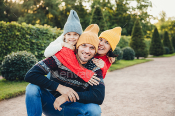 Handsome man has good relationship with wife and small daughter who embrace him from back / Photodune, Misc