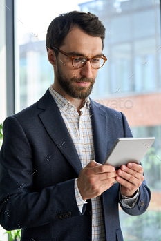 Serious mature bearded businessman using tablet device standing in office. / Photodune, Misc