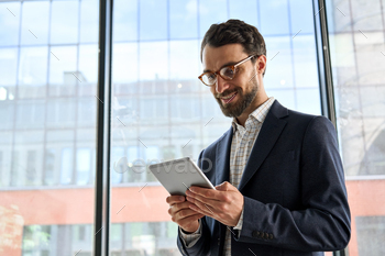 Smiling mature bearded businessman holding tablet device standing in office. / Photodune, Misc