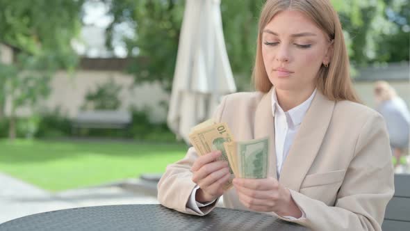 Young Businesswoman Counting Dollars in Outdoor Cafe