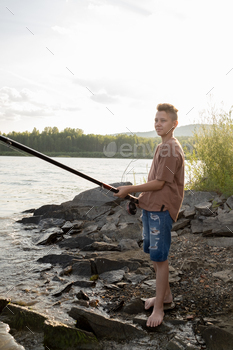 釣りをしながら水辺に立っている長いロッドを持つアクティブな10代の少年 / Photodune, Misc
