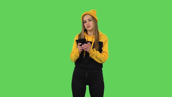 Modern Girl in Yellow Hat Is Texting on Her Phone. Green Screen