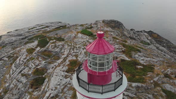 Slow aerial orbit of red bricklight lighthouse in Norway as the sun starts to go down