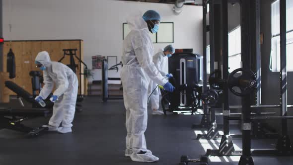 Team of health workers wearing protective clothes cleaning gym by using disinfectant sprayer