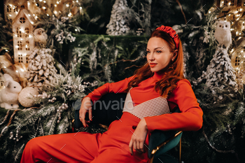赤いスーツを着た女の子がクリスマスの背景の近くの椅子に座っています。上の赤い女性 / Photodune, Misc