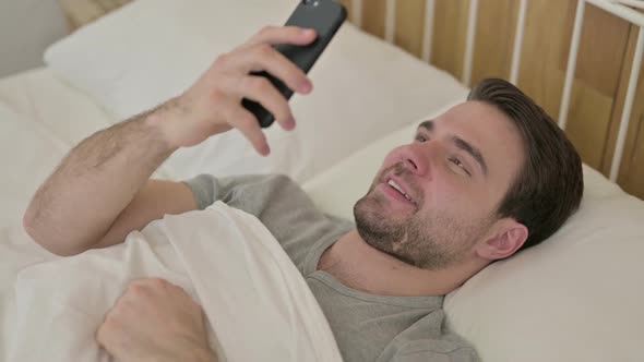 Beard Young Man Doing Video Chat on Smartphone in Bed