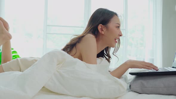 Beautiful Attractive Asian young woman lying on bed and using computer laptop