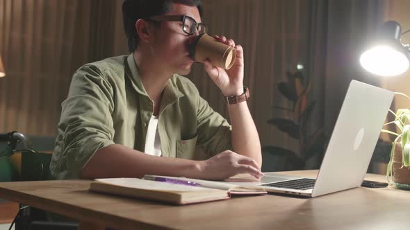 Asian Man Sitting In A Wheelchair While Working On Laptop Computer And Drinking Coffee At Home