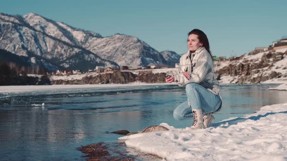 Woman Tourist Sits on the Bank of a River in a Mountainous Area