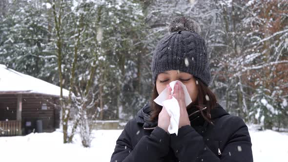 Female blowing her nose on cold winter day in forestry area during snowfall