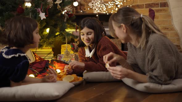 Mom and Two Daughters Having Good Times Together Eating Mandarines Under Christmas and Talk