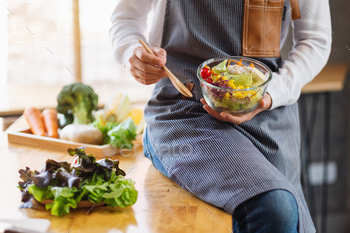 a woman cooking and holding a bowl of fresh mixed vegetables salad to eat in kitchen / Photodune, Misc