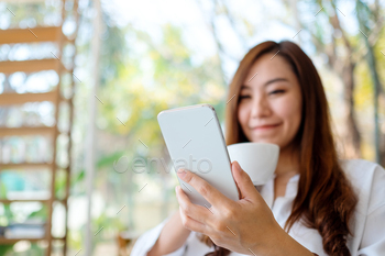 カフェでコーヒーを飲みながら携帯電話を持って使用している美しいアジアの女性 / Photodune, Misc