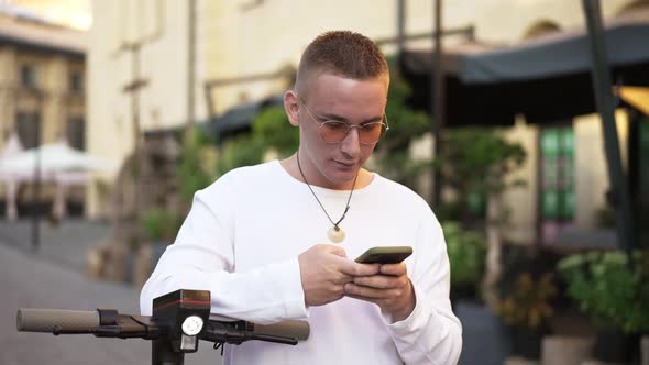 Medium Shot Portrait of Relaxed Confident Caucasian Young Man in Sunglasses Messaging Online on