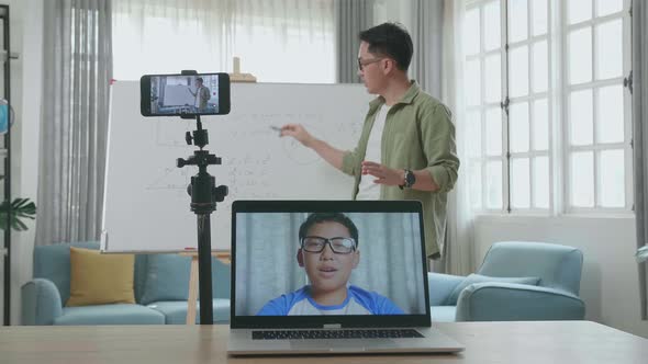 Asian Male Teacher Teaching Math Online At Home With Boy Student On Laptop Screen