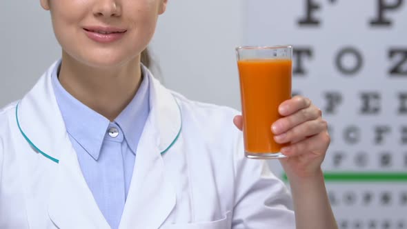 Smiling Female Doctor Showing Carrot Juice Against Eye Chart Background
