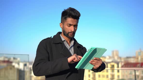 Young Concentrated Man Surfing Social Media on Tablet Looking Away Thinking Standing Outdoors