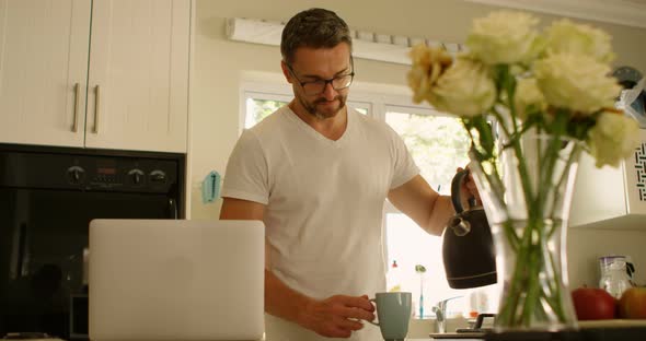 Man pouring water into coffee cup in kitchen 