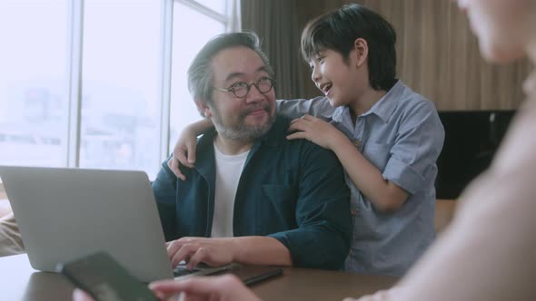 asian male dad using laptop and conversation on smartphone remotely distance working