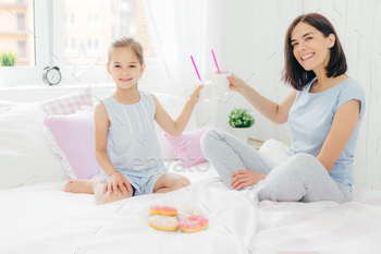 きれいな女性と彼女の娘はベッドでカクテルとグラスをチリンと鳴らし、寝室で朝食をとる / Photodune, Misc