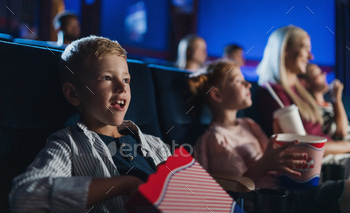 家族と一緒に座って映画館で映画を見たり、ポップコーンを食べたりする小さな男の子 / Photodune, Misc