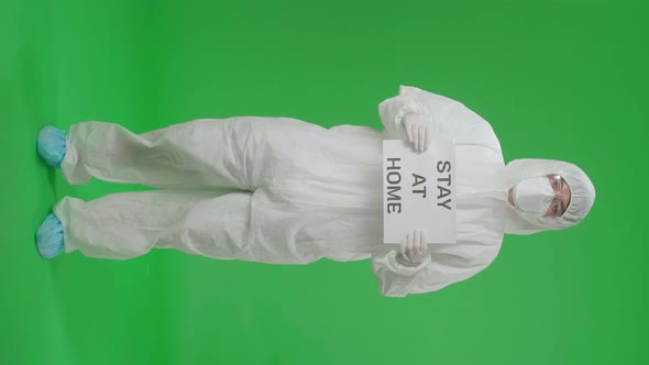 Man Wearing Protective Uniform PPE And Holding Stay At Home Sign In The Green Screen Studio