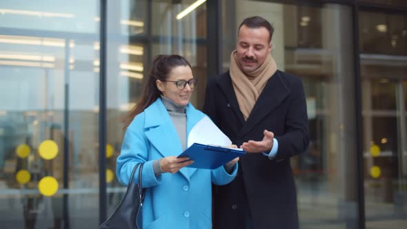 Businesspeople Outside Business Center Holding Clipboard with Documents Plans and Discussing