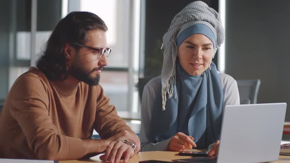 Businesswoman in Hijab Speaking with Male Colleague in Office