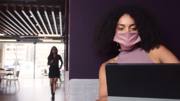 Businesswoman Wearing Mask Working In Socially Distanced Cubicle In Office During Health Pandemic