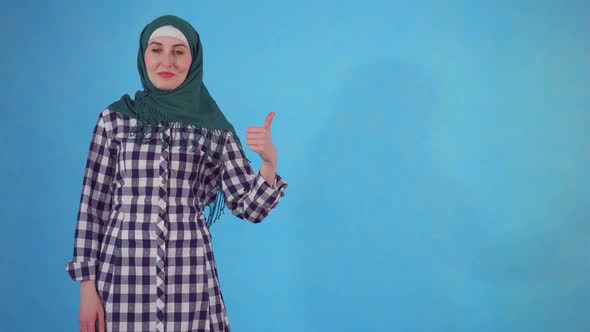 Young Muslim Woman Showing Thumbs Up on a Blue Background