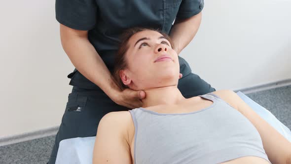 Massagist Working with Young Woman's Neck While She Is Lying on a Couch