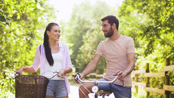 Happy Couple with Bicycles Talking at Summer Park