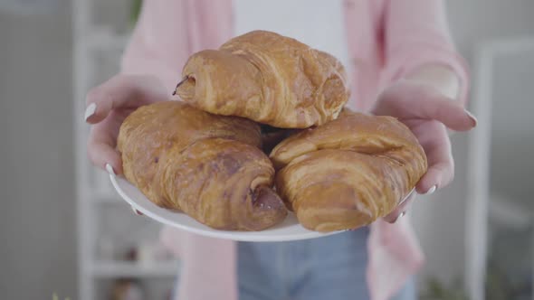 Female Hands Showing Plate with Tasty Fresh Croissants at Camera