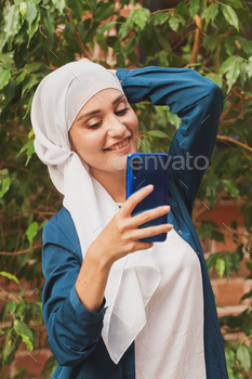自撮りをしているイスラム教徒の女性。スカーフと幸せな美しい女の子を使用して自分の写真を撮る / Photodune, Misc