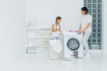 Happy mother and daughter stand near washing machine, girl pours liquid powder / Photodune, Misc