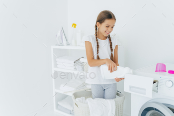 小さな愛らしい忙しい女の子が洗濯かごに立って、洗濯機のコンパートメントに洗剤を注ぐ / Photodune, Misc