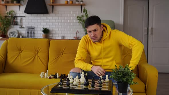 Young Man Sitting on Yellow Sofa and Playing Chess in Room