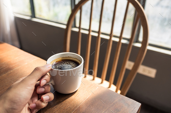 カフェのヴィンテージの木製テーブルに白いホットコーヒーカップを持っている手のクローズアップ画像 / Photodune, Misc