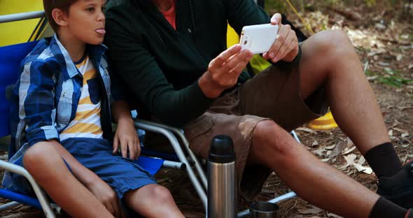 Father and son taking a selfie on mobile phone outside tent