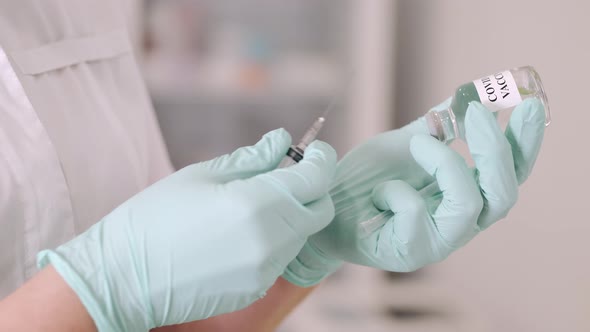 A Female Doctor in Blue Protective Gloves Holding a Medical Syringe and Vial