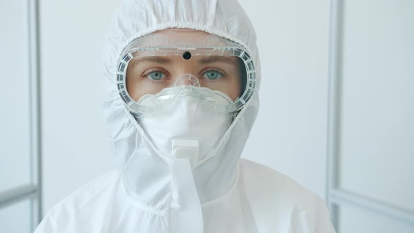 Portrait of Young Doctor in Protective Goggles, Respirator and Suit Standing in Clinic