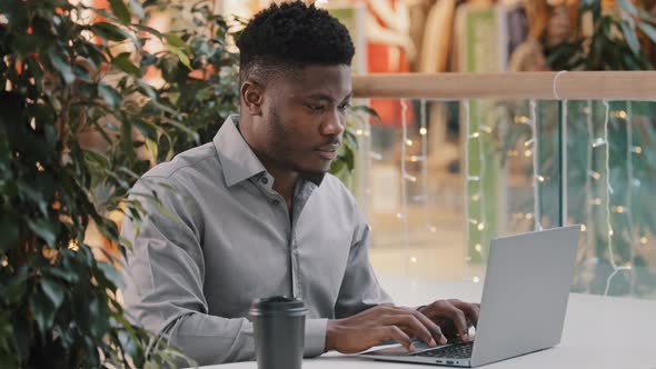 Focused Young African American Male Freelancer Carefully Looking at Laptop Screen Working Remotely