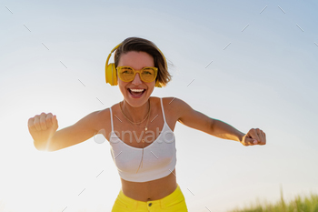 happy smiling woman listening to music in colorful yellow headphones on sunny beach in summer / Photodune, Misc