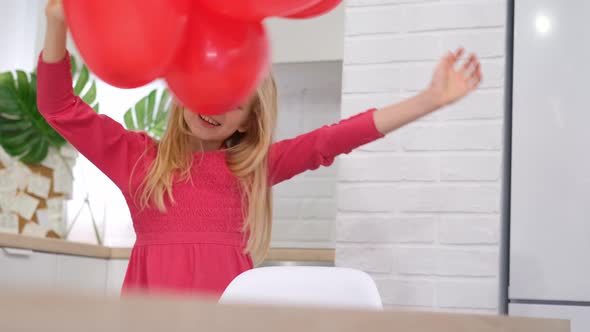 Little Blonde Girl Dancing with Red Heart Shape Balloons at Home