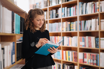 Beautiful girl is studying reading a book while standing on the floor among books in the bookshop / Photodune, Misc